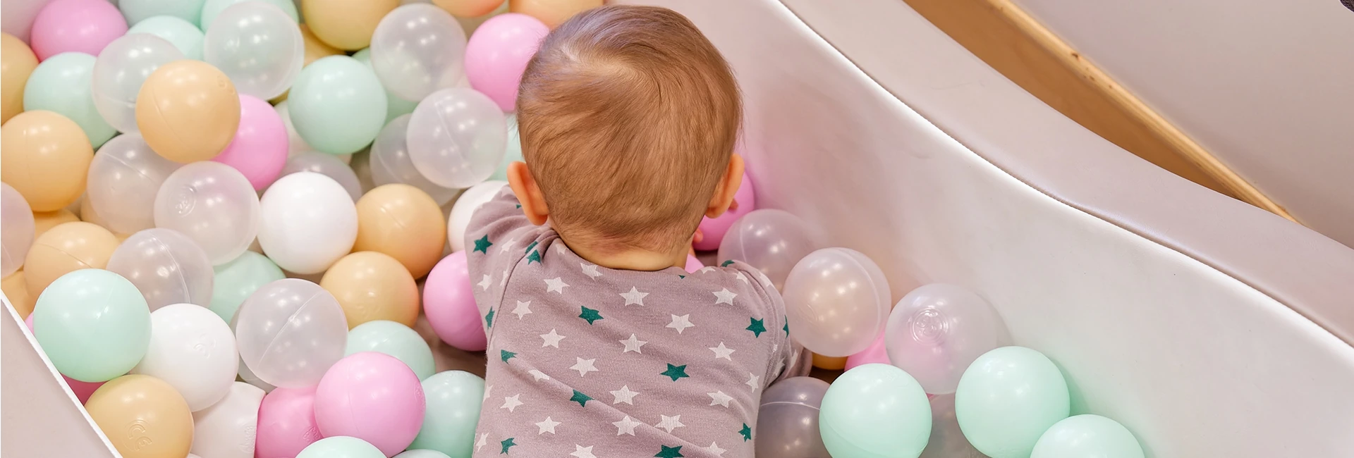 Un bébé joue dans un parc à balles en plastique de couleurs pastel