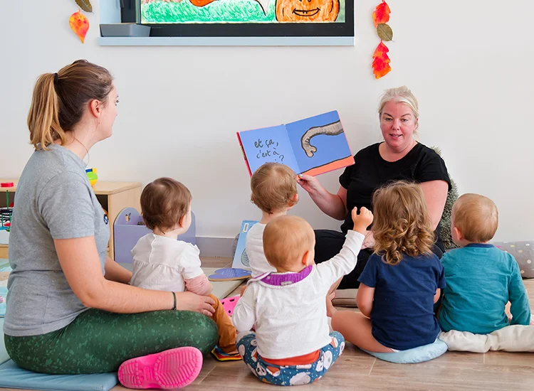 Deux professionnelles de la petite enfance lisent un livre illustré à un groupe de 5 enfants