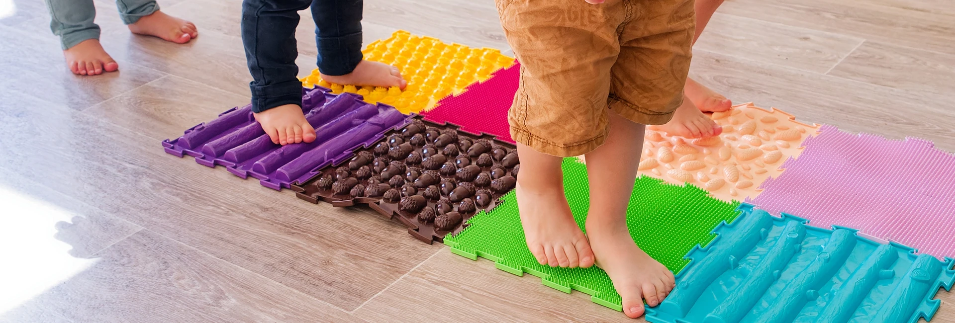 Des enfants pieds nus marchent sur des plaques de différentes textures pour appréhender différentes sensations