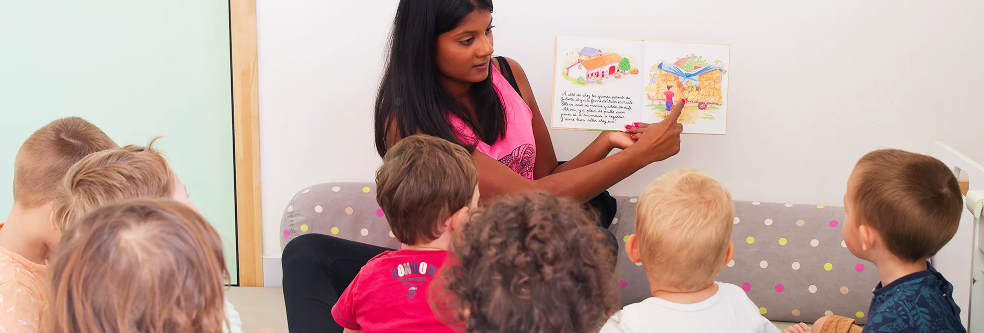 une auxiliaire de puériculture s'occupe d'un groupe d'enfants et les occupe en leur lisant un livre illustré